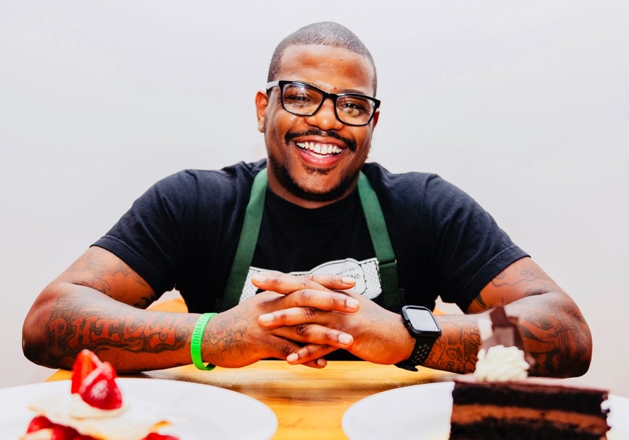 Chef Elijah Miligan sitting and smiling at a table with hands crossed